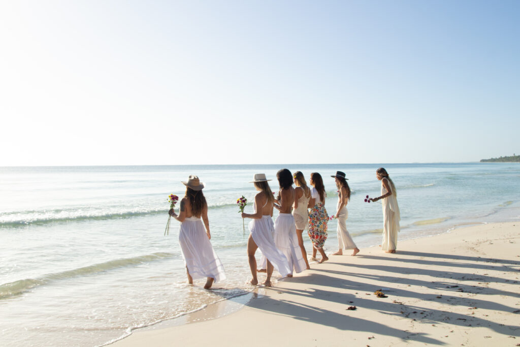 a group of women in white dresses walking on a beach