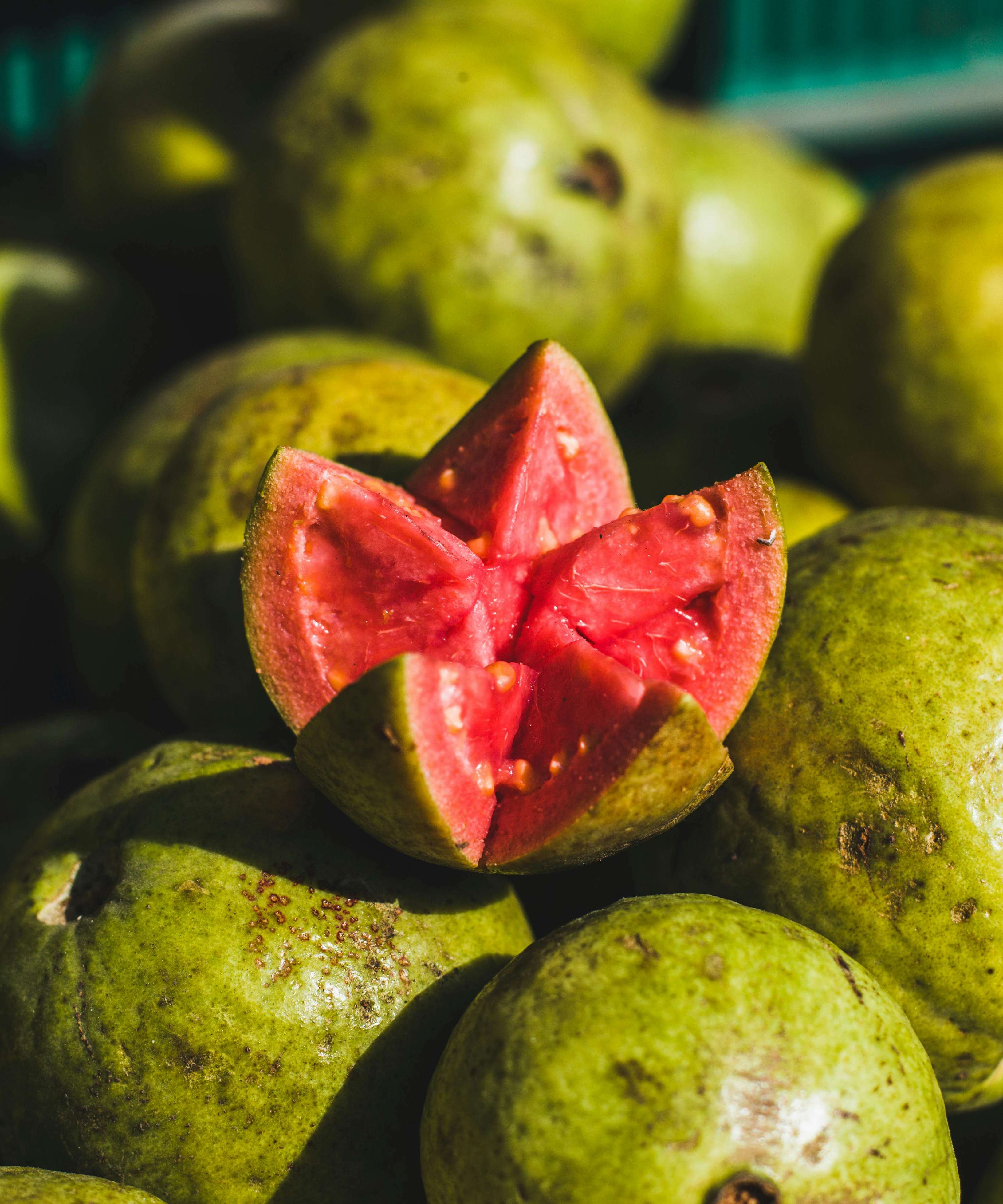 A pile of ripe green guavas with a vibrant pink sliced guava on top, highlighting freshness.