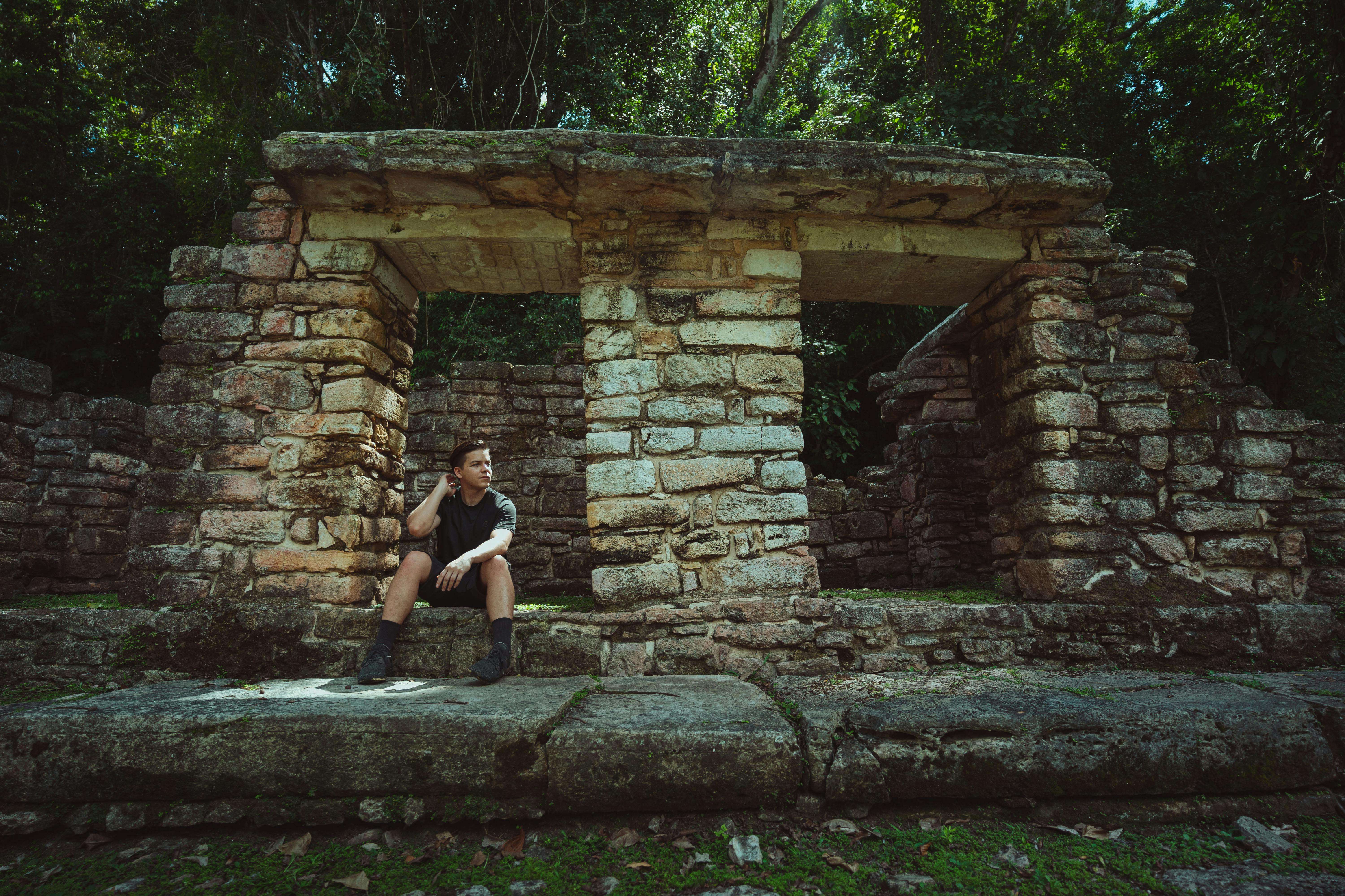 A man sits on ancient stone ruins in a lush jungle, perfect for travel and adventure themes.