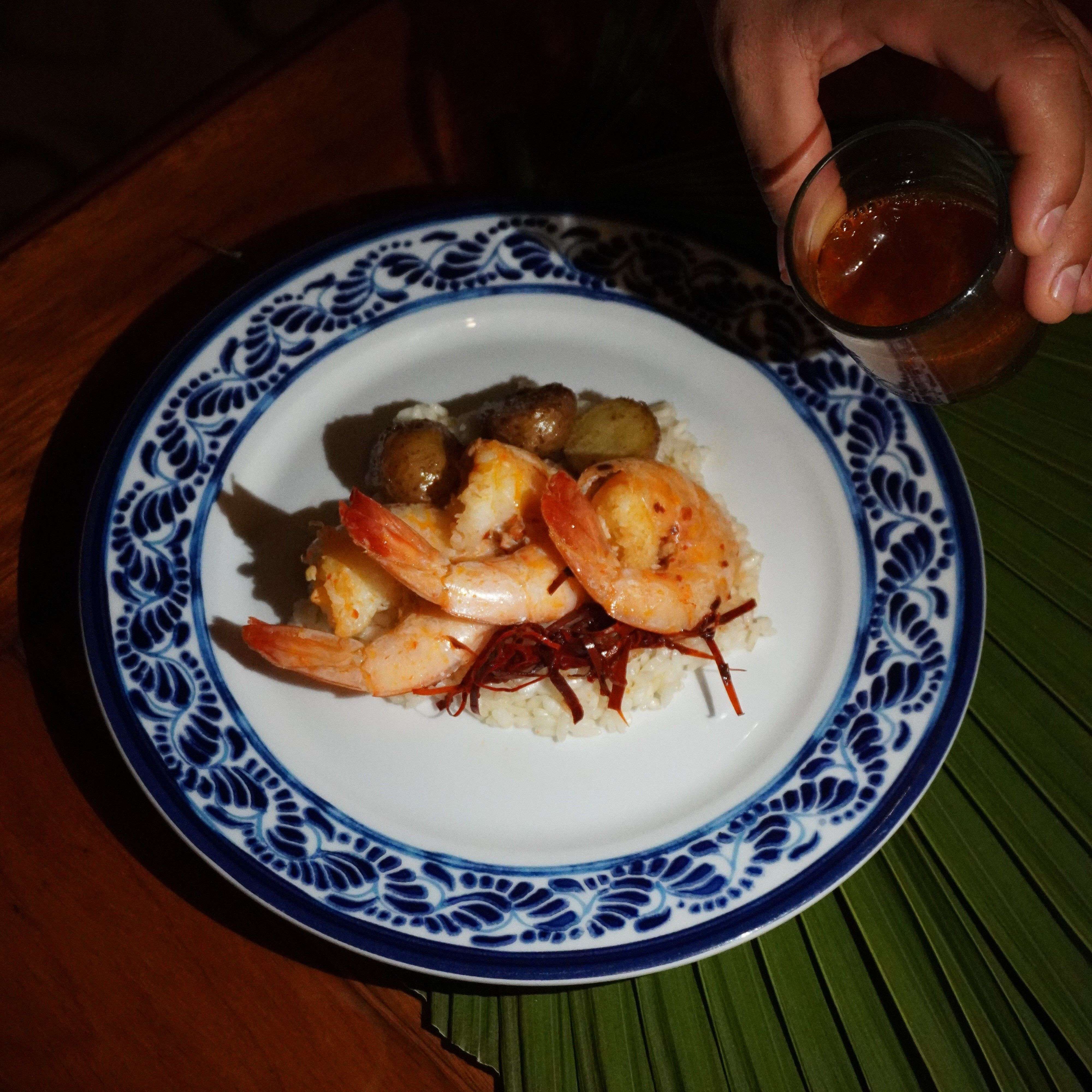 Plate of shrimp served over rice with vegetables, garnished with sauce being poured.