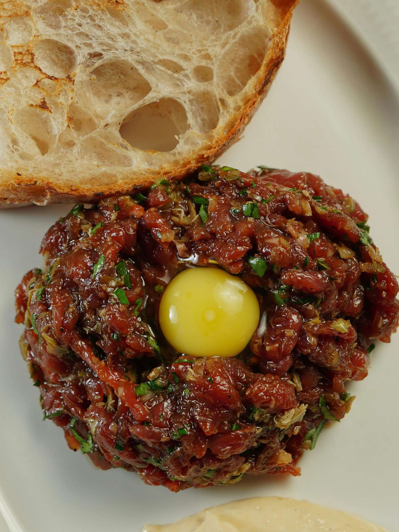A gourmet steak tartare dish topped with a fresh yolk, served with artisan bread.