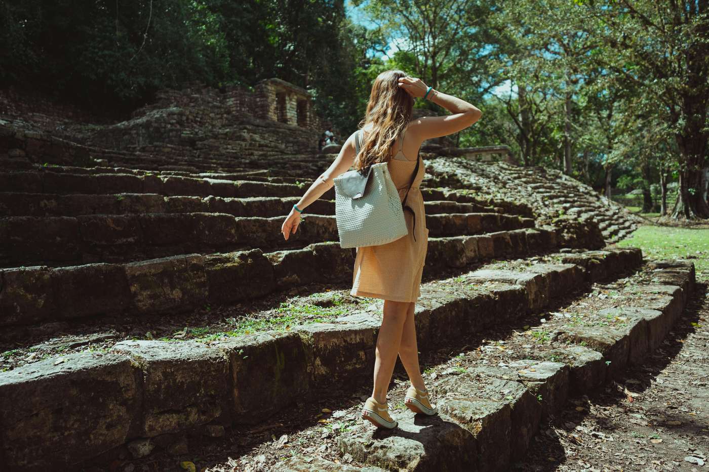 A woman with a backpack exploring ancient Mayan ruins outdoors, surrounded by nature.