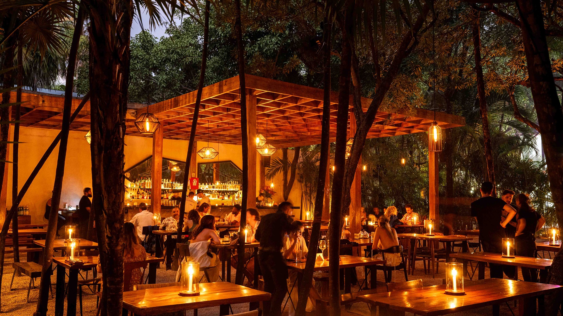Candlelit tables under a wooden pergola in the jungle at ARCA restaurant in Tulum