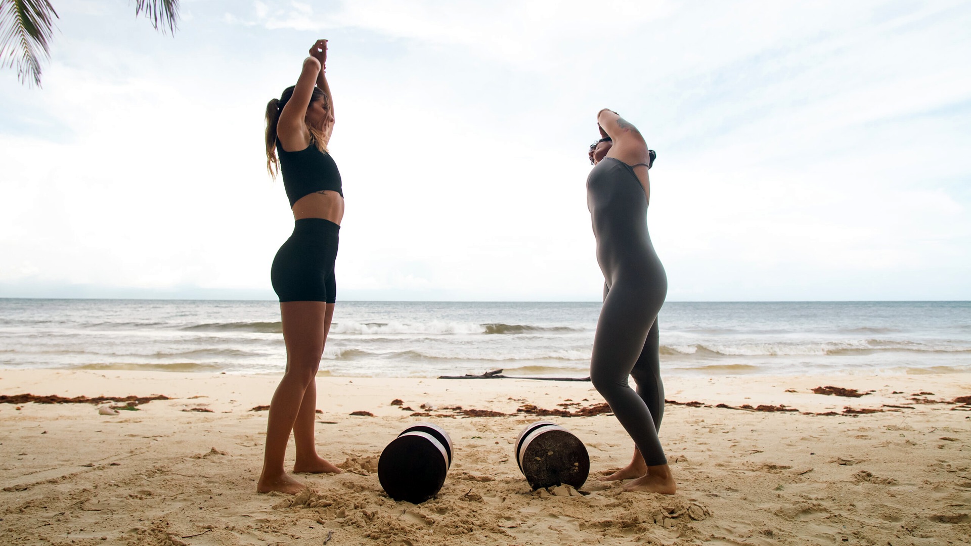 Two guests stretching on the beach in front of Casa Nalum during a morning workout