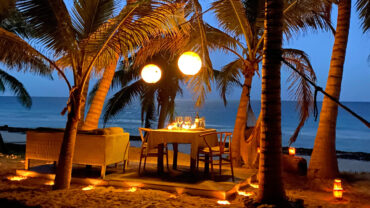 A candlelit table for dinner under palm trees on the beach at Casa Nalum at dusk, Sian Ka'an, Tulum