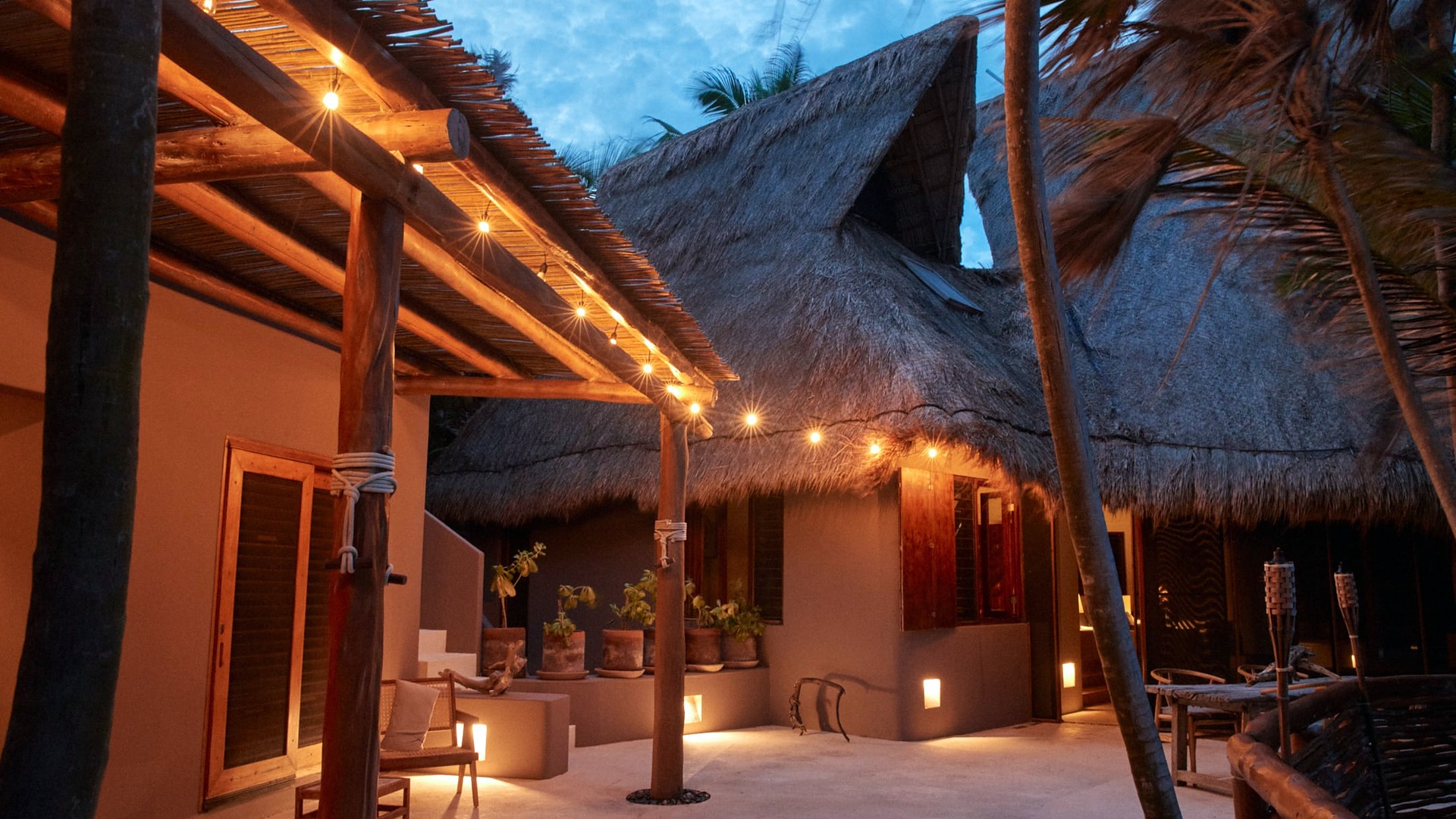 The lantern-lit courtyard and thatched palapa roofs of Casa Nalum at dusk