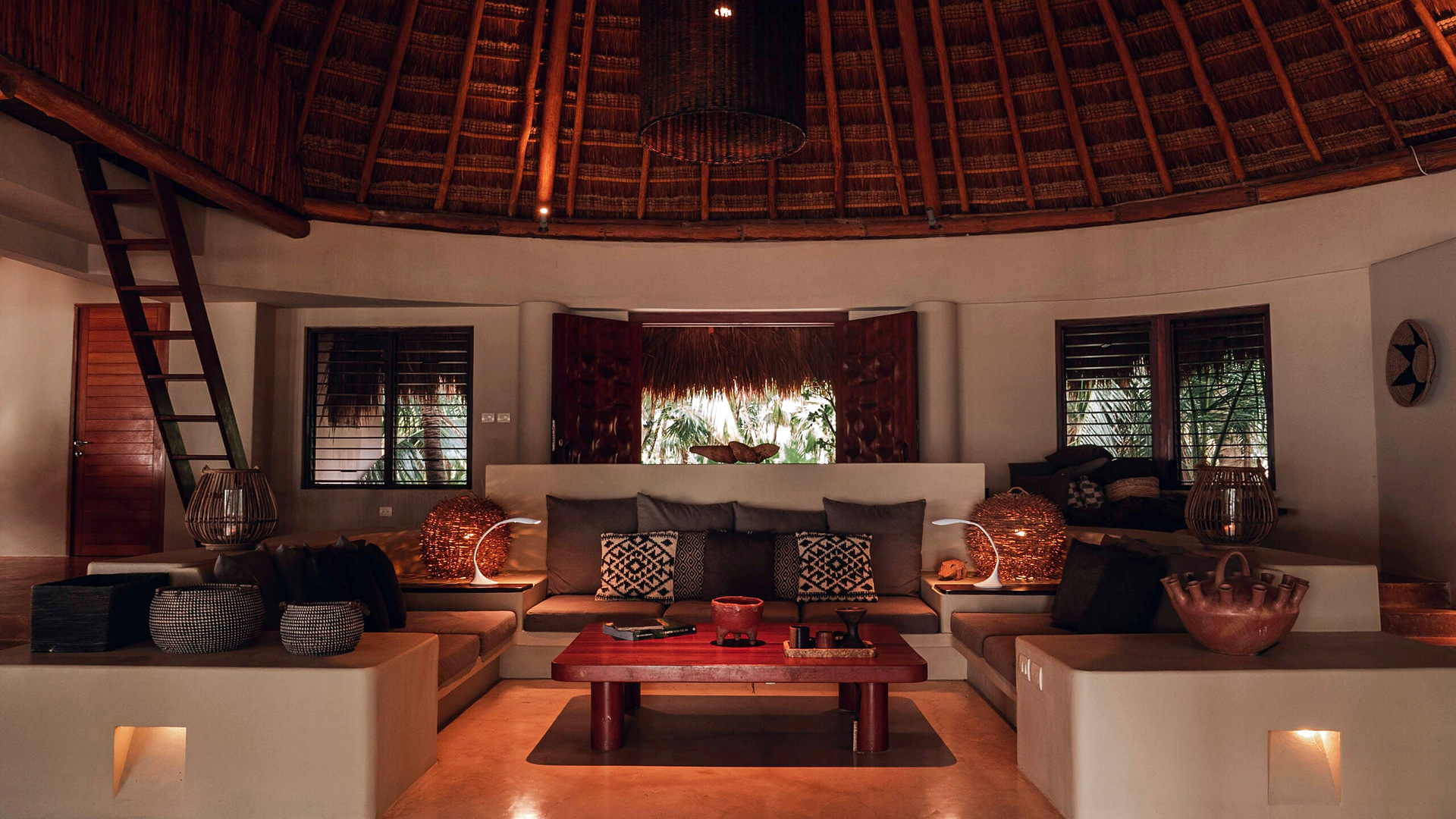 The palapa living room at Casa Nalum with built-in sofas, cushions, and warm lamps under a thatched roof