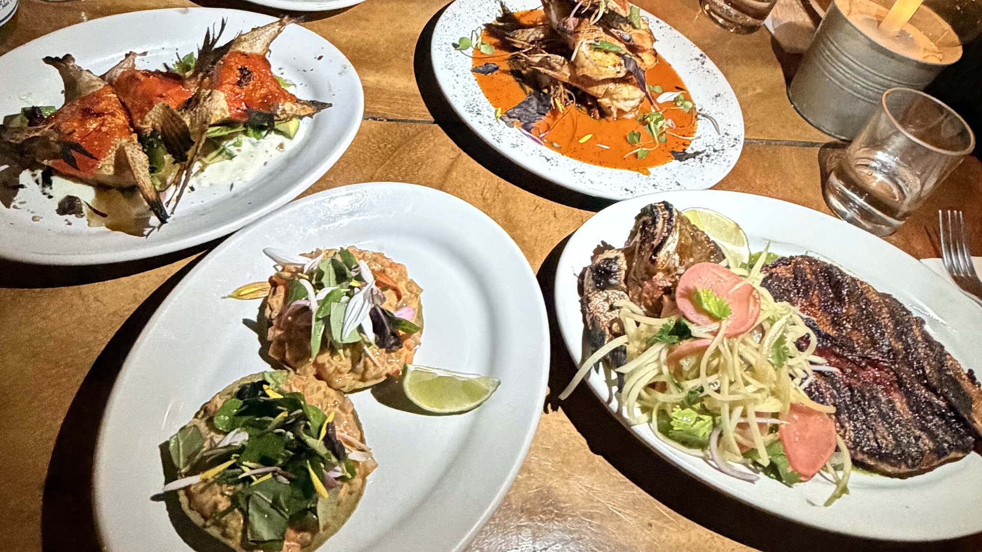 Shared plates of grilled fish and tostadas on a table at Hartwood in Tulum